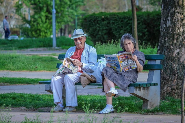 Deux personnes en maison de retraite sur un banc en train de lire le journal.