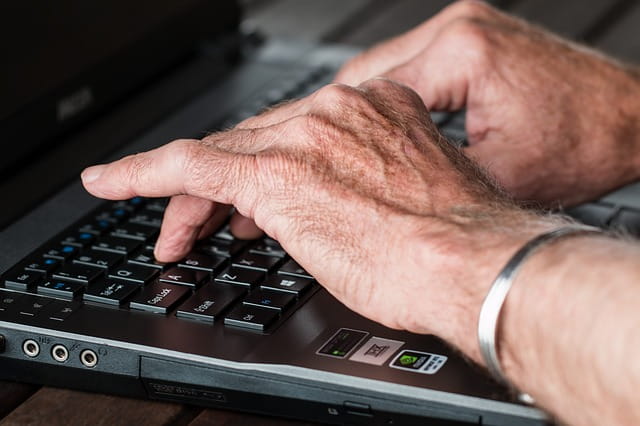 Les mains d'un senior qui tape un texte sur un ordinateur.