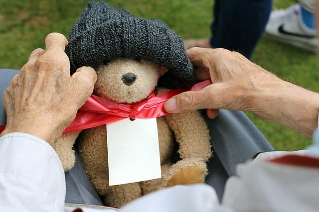 Mains d'un senior tenant un ours en peluche dans une maison de retraite.