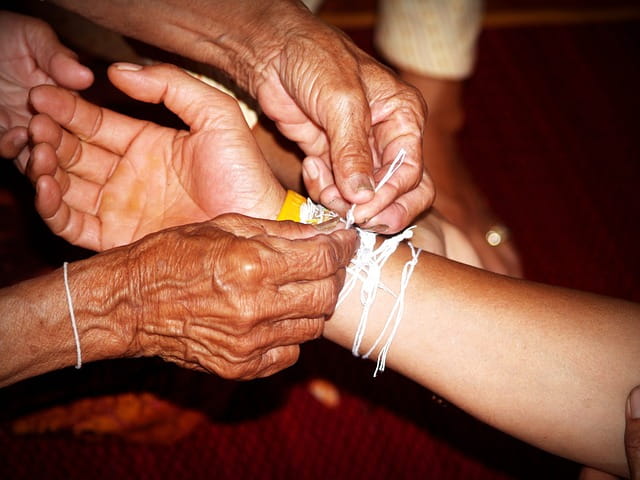 Mains d'une personne âgée accrochant un bracelet au poignet d'une jeune fille.
