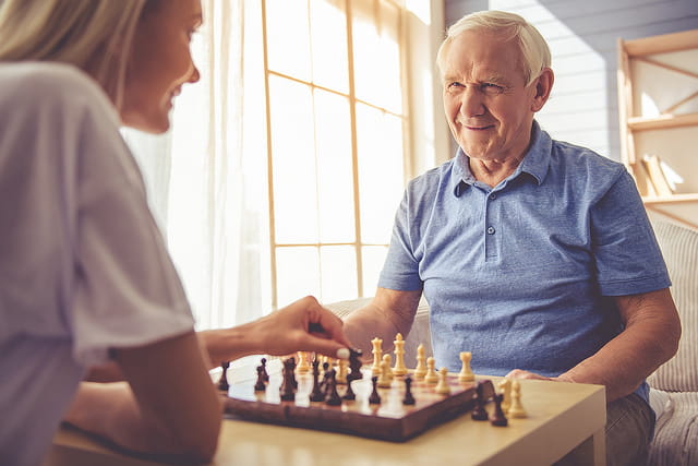 Femme qui joue aux échecs avec un homme âgé en maison de retraite.