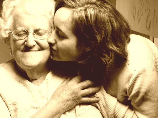 Jeune fille qui embrasse sur la joue une femme âgée en maison de retraite.
