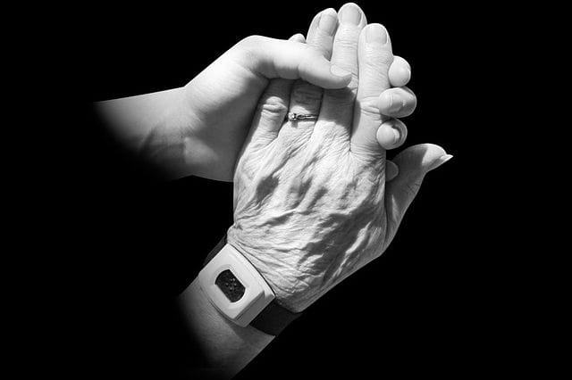 Main d'une personne âgée soutenue par la main d'un aidant.