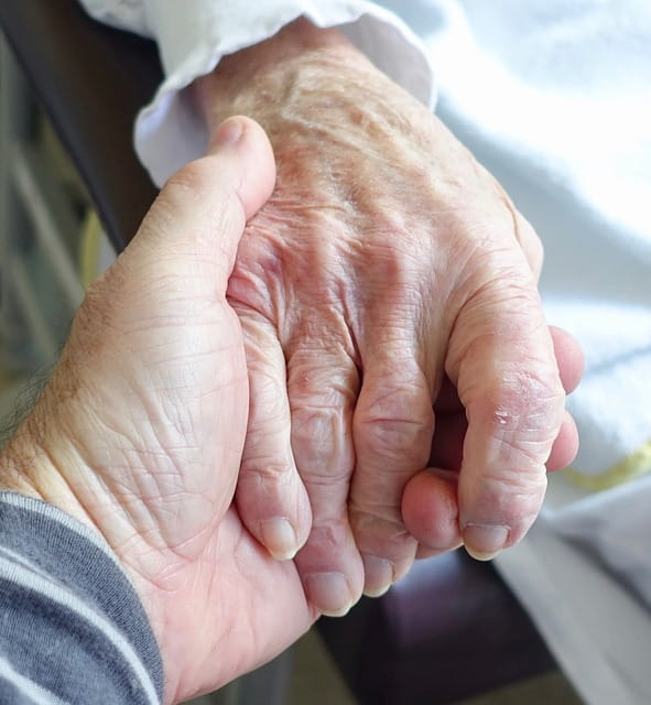 Une main de personne âgée tenue par un employé de maison de retraite.
